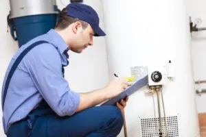 Plumber inspecting water heater and taking notes on maintenance checklist.