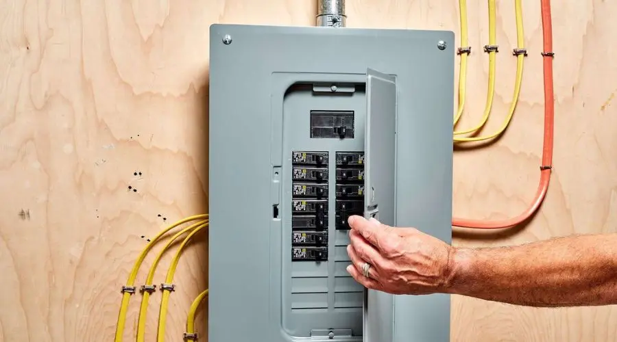 Hand interacting with an electrical panel and organized circuit breakers on a wooden wall.