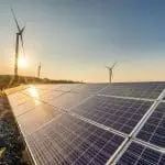 Solar panels and wind turbines in a lush landscape at sunset, highlighting renewable energy for The Meridian Company.