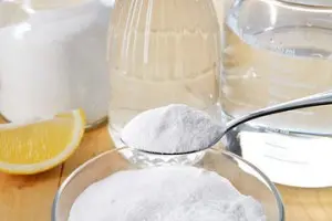 Spoonful of baking soda above a bowl, with vinegar, water, and lemon, illustrating DIY solutions for garbage disposal odors in home maintenance.