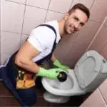 A man in blue overalls cleans a toilet with a plunger, promoting home hygiene for The Meridian Company's services.