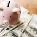 Pink piggy bank with coin slot and stack of money, illustrating financial savings for home maintenance and energy tips.
