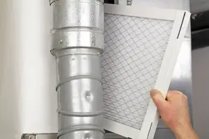 Hand removing a furnace filter from a ventilation system, emphasizing furnace maintenance and home service solutions by The Meridian Company.