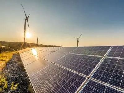 Solar panels and wind turbines at sunset, representing sustainable energy sources for homeowners and the benefits of renewable energy.