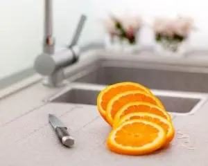 Sliced oranges on a kitchen countertop with a knife and sink, illustrating fresh food preparation related to home maintenance and plumbing solutions.