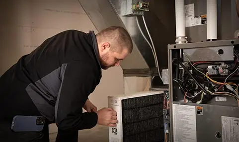 Technician servicing HVAC system, replacing air filter, ensuring optimal heating performance for home comfort services by The Meridian Company.