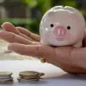 Hand holding a piggy bank with coins stacked, representing financial savings for HVAC maintenance in Lansing, MI.