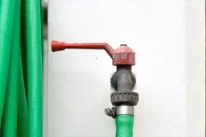 Close-up of a garden hose faucet with a red handle, surrounded by green garden hoses, illustrating home maintenance plumbing solutions.