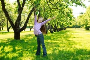 Child joyfully playing outdoors in a green park with trees, symbolizing the importance of clean air and a healthy environment.