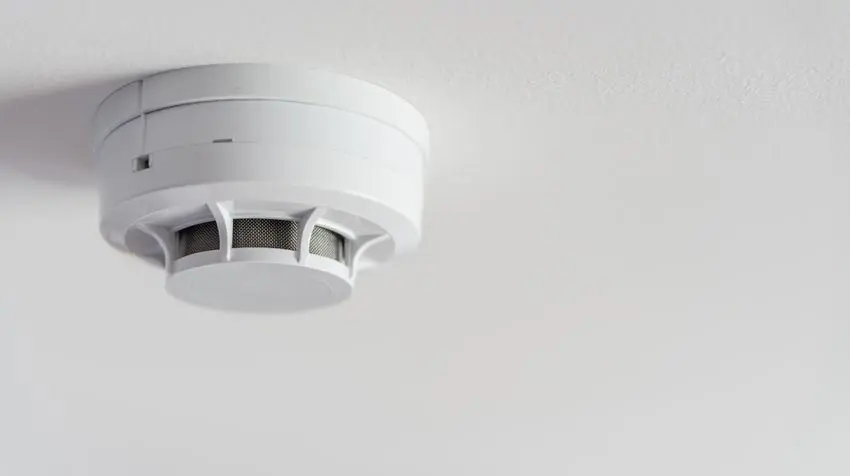 Smoke detector mounted on ceiling, emphasizing home safety and fire prevention services offered by The Meridian Company in East Lansing, MI.