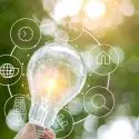 Light bulb glowing in hand with icons, symbolizing innovation in electrical services by The Meridian Company.