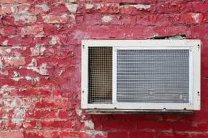Old air conditioning unit mounted on a red brick wall, highlighting HVAC equipment relevant to heating and cooling services.