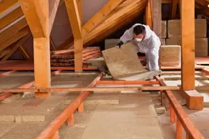 Person installing insulation in attic to improve home energy efficiency and address uneven cooling issues.