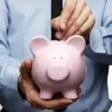 Person in formal attire inserting money into a pink piggy bank, representing financial planning for home services.