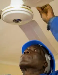 Technician adjusting ceiling fan for improved energy efficiency during winter heating.