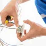Electrician's hands using a screwdriver on electrical components for HVAC maintenance and home comfort solutions.