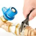 A hand using an adjustable wrench on a valve with brass plumbing parts, showcasing home maintenance by The Meridian Company.