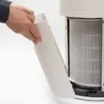 Air purifier with a hand removing the filter, showcasing indoor air quality maintenance by The Meridian Company.