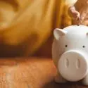 White piggy bank on wooden surface with coin slot; represents saving for plumbing and electrical service maintenance.
