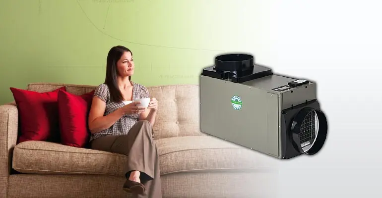 Woman sitting on a couch holding a cup, with a dehumidifier prominently displayed, illustrating indoor air quality improvement and HVAC services offered by The Meridian Company in Lansing and East Lansing, MI.