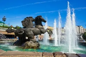 Horse statue fountain surrounded by water jets in a vibrant public space, representing decorative landscaping and urban design.