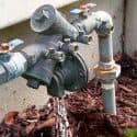 Water meter and piping system with visible valves and water leakage near mulch, showcased by The Meridian Company.