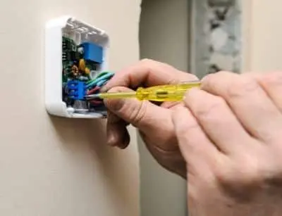 Person using a screwdriver to install a Wi-Fi programmable thermostat on a wall, emphasizing HVAC system maintenance and energy efficiency.