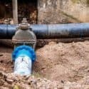 Water pipe and valve in dirt terrain, featuring metal and blue plastic elements for home services maintenance in Lansing.