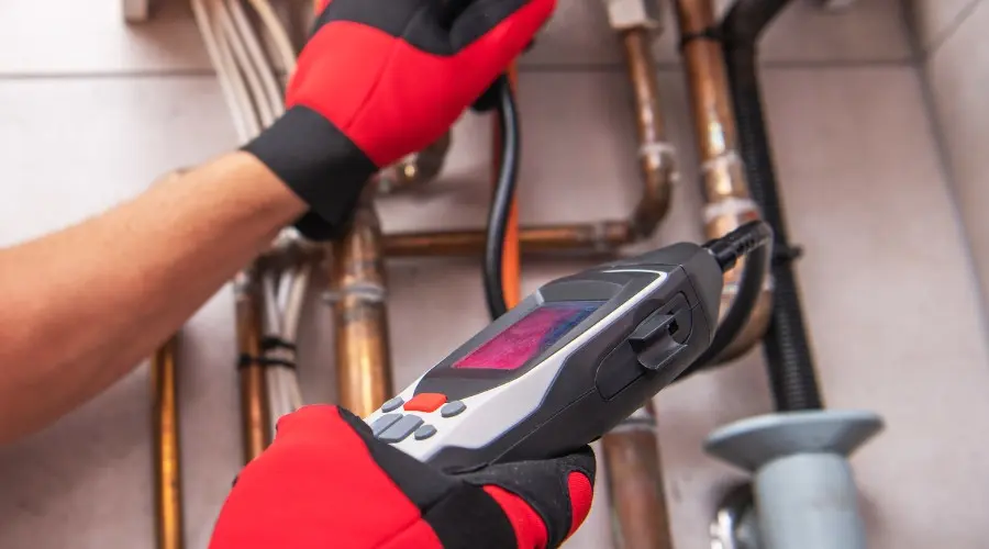 Technician using gas leak detection tool on plumbing pipes, highlighting safety measures for identifying gas leaks.