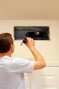 Man inspecting air ducts with a flashlight, addressing uneven cooling issues in home maintenance.