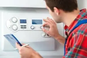Technician adjusting boiler control panel while holding clipboard, illustrating HVAC service and boiler maintenance.
