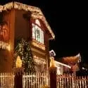 Festively decorated residential house with Christmas tree, icicle lights, and lawn decorations for winter ambiance.