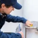 Technician in blue uniform using a measuring device near plumbing tools at City Plumbing service location.