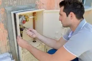 Plumber inspecting water meter and pipes for foundation leak detection.