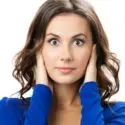 Woman with dark hair covering her ears, in a blue top, represents water heater noise issues for City Plumbing services.