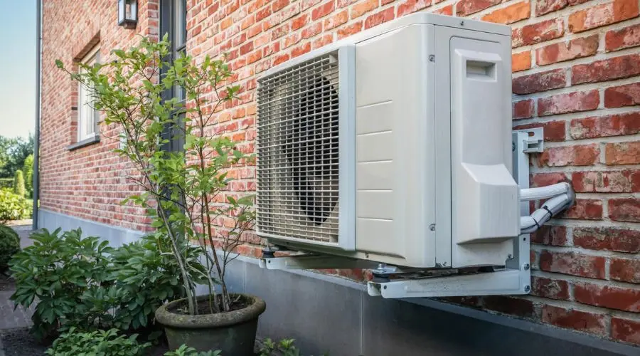 Modern air conditioning unit on a brick wall with a potted plant, showcasing City Plumbing’s heating and cooling solutions.