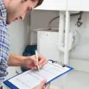 A man inspecting plumbing supplies with clipboard and pen for maintenance tasks related to City Plumbing services.