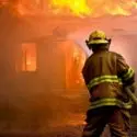 Firefighter in gear battling flames at a burning building, representing emergency service response by City Plumbing.