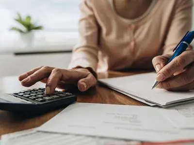 Person using a calculator and writing notes on paper, illustrating financial planning related to energy-efficient home improvements under the Inflation Reduction Act.