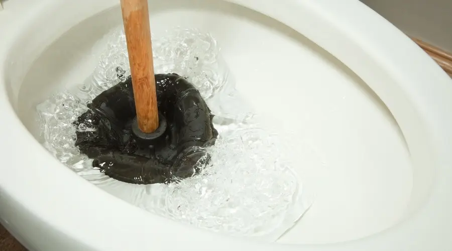 Toilet with plunger in water, illustrating clogged toilet repair and maintenance tips for preventing clogs.