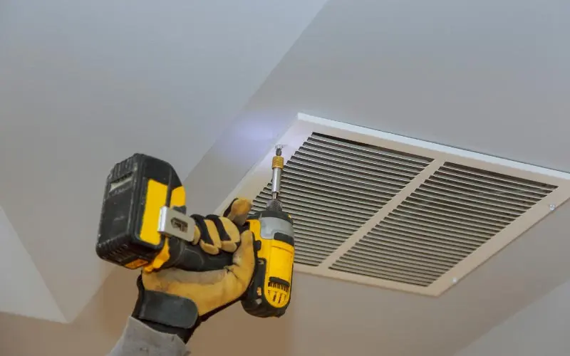 Technician using a power drill to install a ceiling vent, emphasizing HVAC maintenance and whole-home ventilation for improved air quality and comfort.