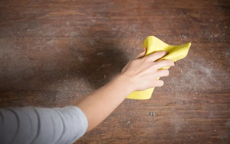Person's hand cleaning a dusty wood floor with a yellow cloth, emphasizing home maintenance and cleanliness for HVAC comfort.