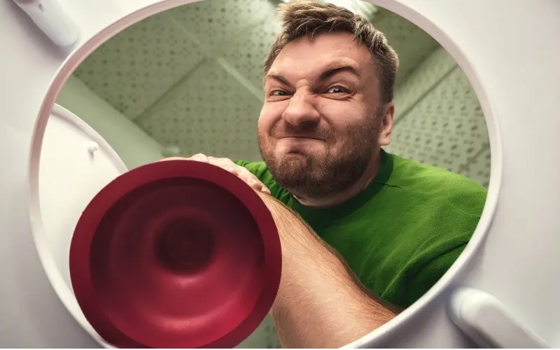 Man using a flange plunger to unclog a toilet, demonstrating proper plunging technique in a bathroom setting.