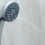 Showerhead with water flowing, illustrating plumbing maintenance and potential water pressure issues related to clogs and installation.