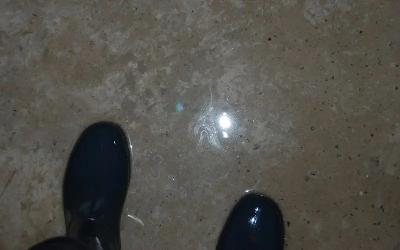 Person wearing rubber boots standing on a concrete floor with visible water pooling, illustrating symptoms of slab leaks in homes.