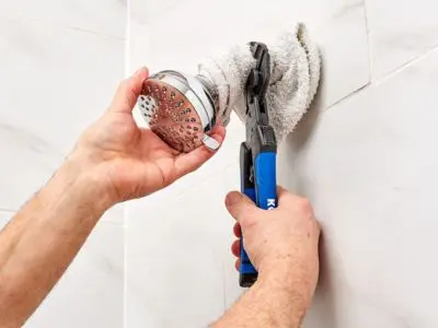 Person inspecting a showerhead with pliers, checking for mineral buildup and clogs, relevant to plumbing maintenance and water pressure issues.