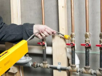Professional using gas leak detector on plumbing pipes with valves, highlighting gas leak detection and repair services.