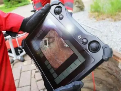 Plumber using a sewer inspection camera monitor to identify blockages and damage in a sewer line, emphasizing advanced plumbing technology for efficient diagnostics.
