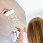 Individual showering under a modern showerhead in a bright bathroom, highlighting Maxwell-White Plumbing's water expertise.