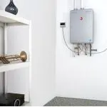 Modern wall-mounted water heater with shelf, brass trumpet, and black device, showcased by Maxwell-White Plumbing.